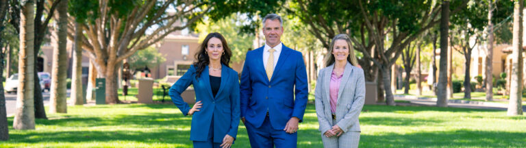 3 Attorneys for the Gill Law Firm posing in front of trees in a park