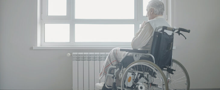 Sad senior man in wheelchair looking out the window, loneliness in old age