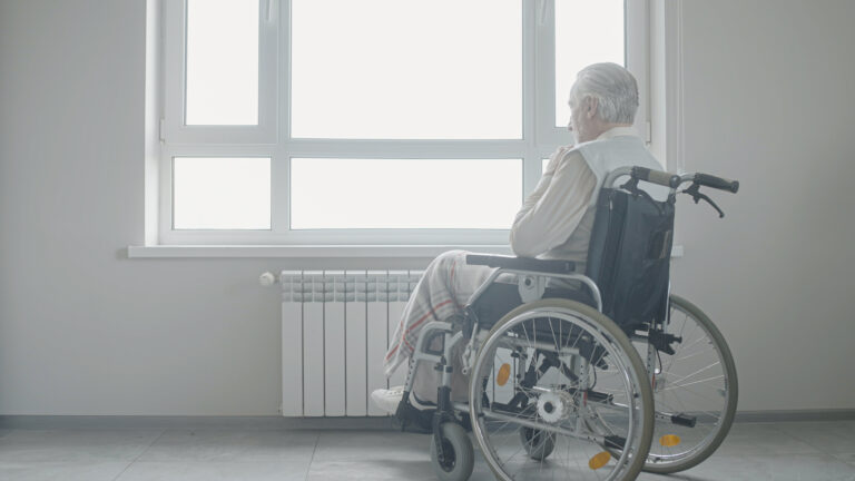 Sad senior man in wheelchair looking out the window, loneliness in old age