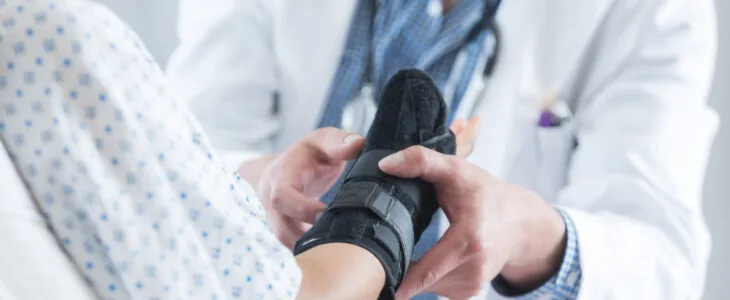 Unrecognizable male doctor places an arm brace on a patient's sprained wrist. The patient is lying in a hospital bed.